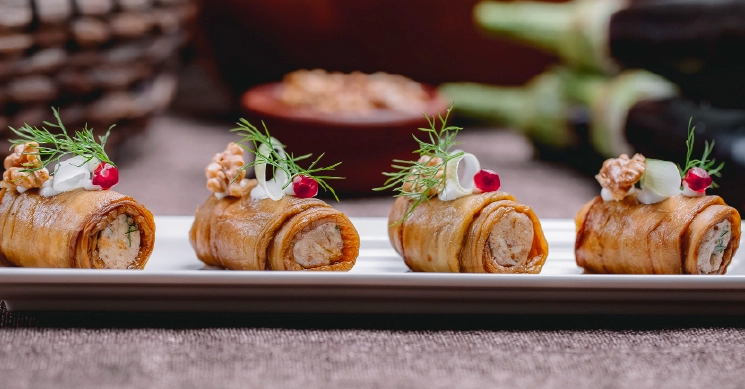 Elegant rolled hors d'oeuvres garnished with herbs, walnuts, and cream, served on a minimalist plate for upscale wedding catering.
